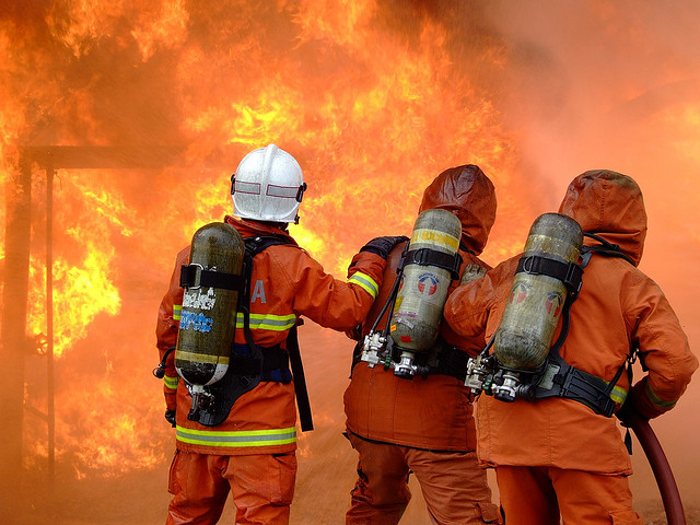 Drei Feuerwehrleute vor einer Flammenwand